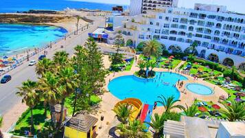 Um resort com uma piscina grande, palmeiras e vista para o mar.