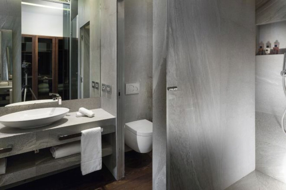 A modern bathroom with a large mirror, a round sink, and a toilet.