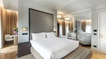 Ein modernes Hotelzimmer mit einem großen Bett, einer Sitzecke mit Stuhl und kleinem Tisch, einem Schminktisch mit Spiegel und einem durchgehenden Türrahmen einsehbaren Badezimmer.