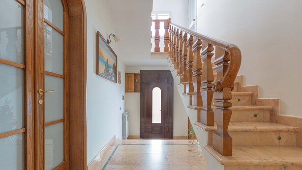 A hallway with a wooden door, a staircase with wooden balusters, and a tiled floor.