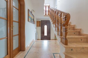 Ein Flur mit einer Holztür, einer Treppe mit Holzspindeln und einem Fliesenboden.