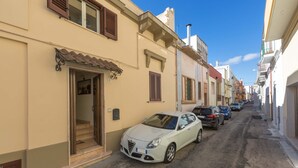 A narrow street lined with buildings, a parked white car, and a visible door entrance.