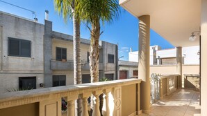 A balcony with a palm tree, a tiled floor, and a view of neighboring buildings.
