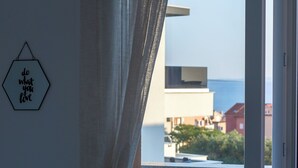 Une pièce avec vue sur des bâtiments et un plan d’eau, vue à travers une fenêtre ouverte.