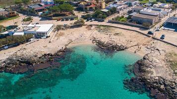 Vista aérea de uma área costeira com águas turquesas cristalinas, litoral rochoso e edifícios residenciais.