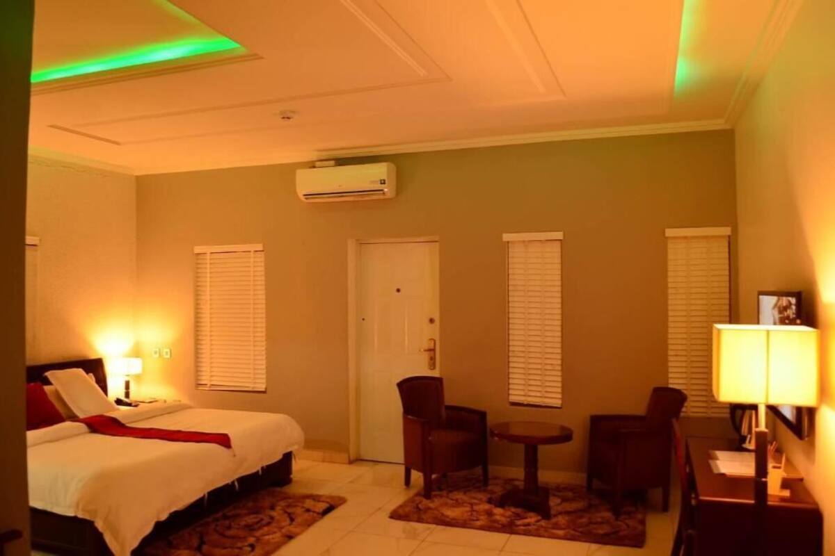 Ein Hotelzimmer mit einem Bett, zwei Stühlen, einem kleinen Tisch, einer Klimaanlage und einer Tür.