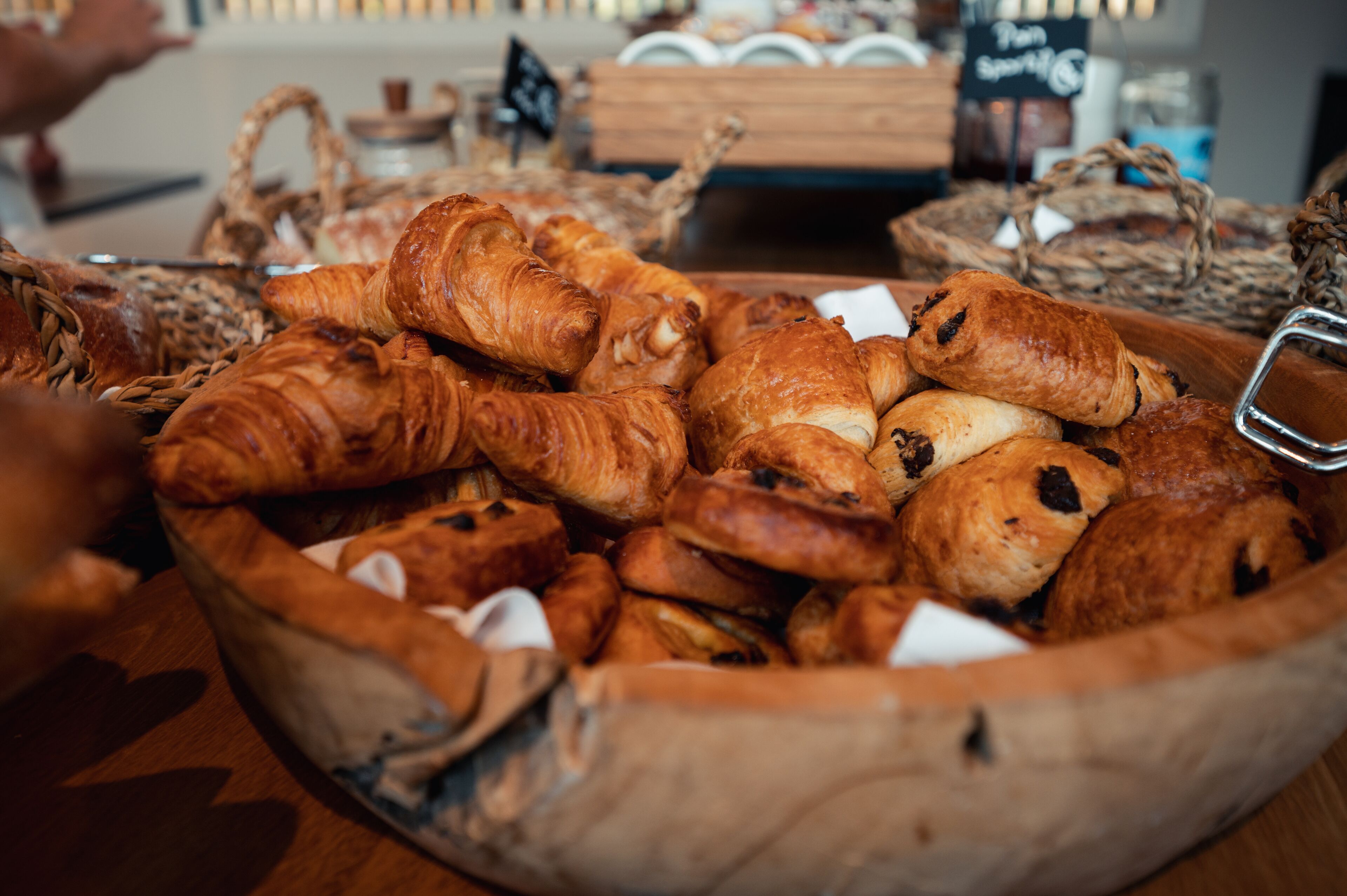 A wooden basket filled with various types of pastries, including croissants and chocolate-filled pastries.