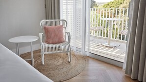 Un balcon avec une chaise et une table blanches, un tapis tissé et une vue sur la verdure.