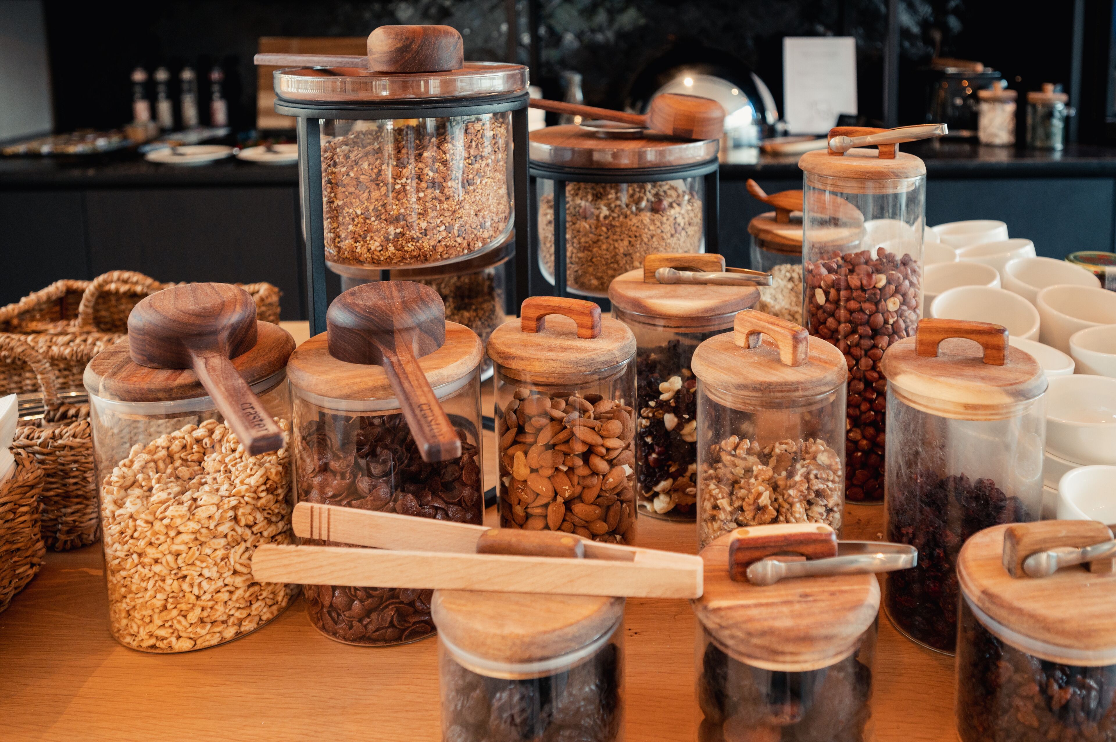 Diversos alimentos en frascos de vidrio con tapas de madera, dispuestos sobre una mesa.