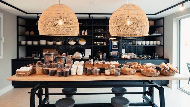 Une cuisine dotée de deux grands luminaires suspendus en osier, d’un plan de travail en bois agrémenté de bocaux et de paniers, et d’étagères remplies d’ustensiles de cuisine.