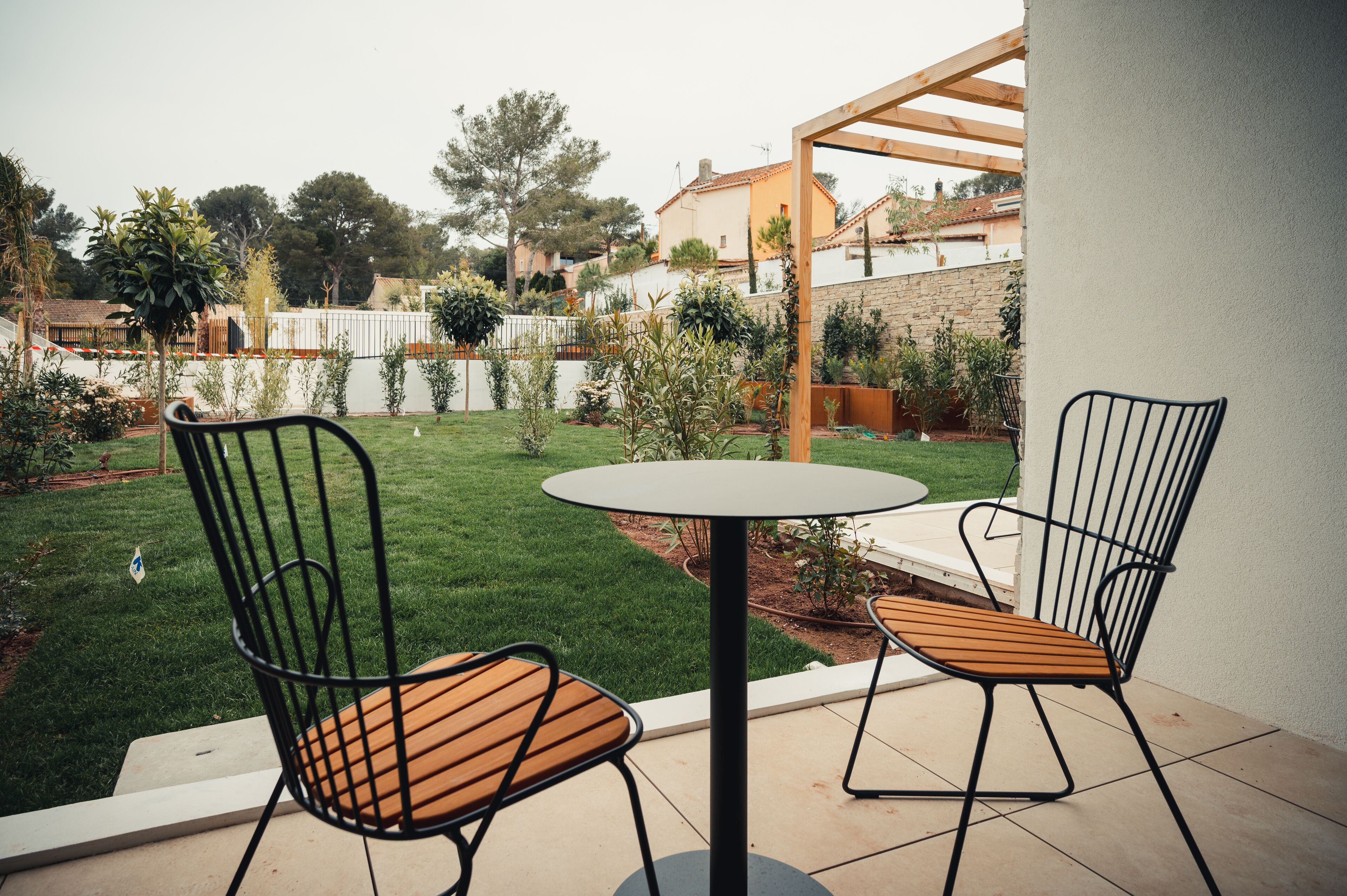 A patio with two chairs and a table, surrounded by a well-maintained lawn and a wooden pergola.