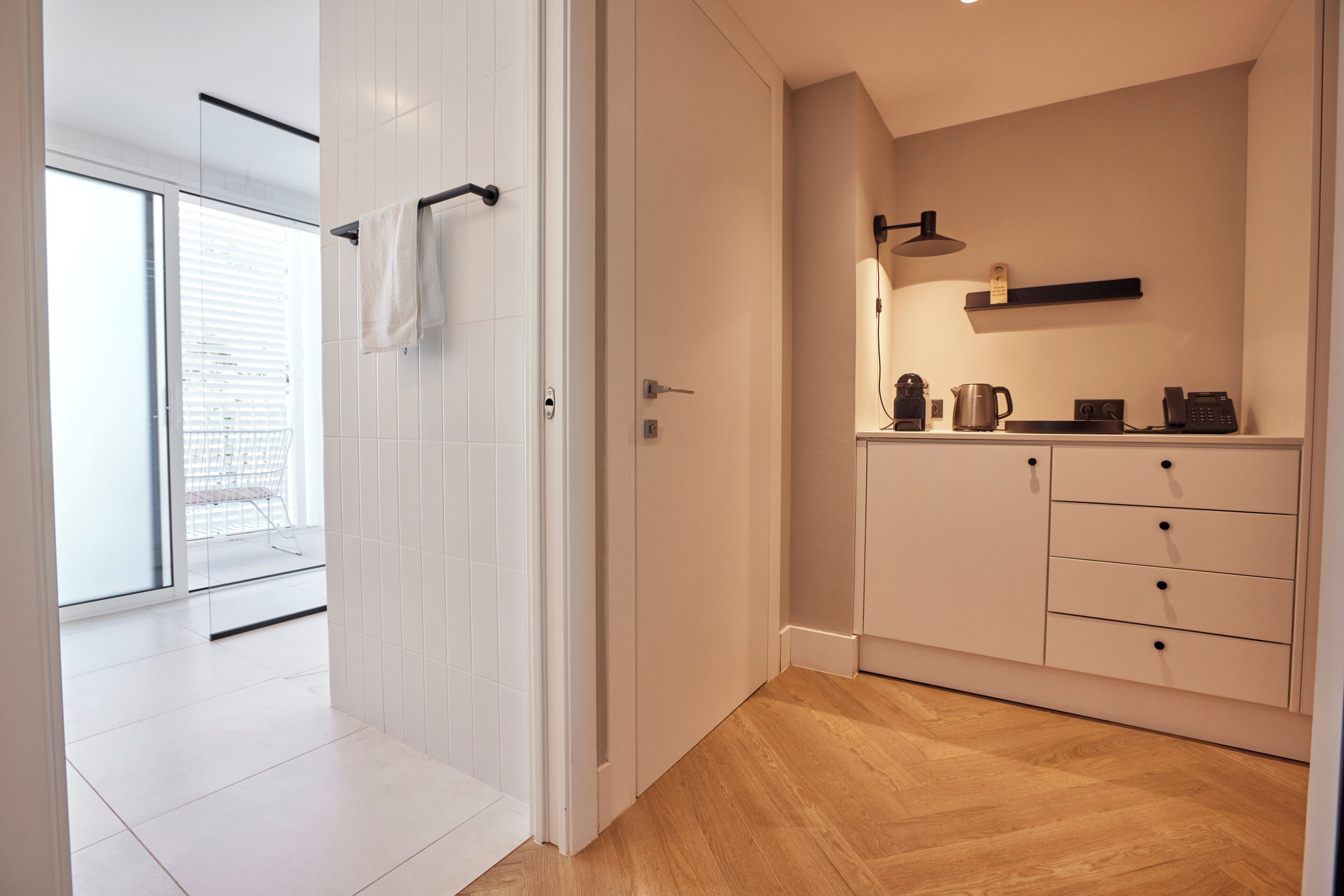Une cuisine moderne avec des meubles blancs, un plancher en bois et une vue sur un balcon, accessible par une porte ouverte.