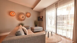 Un salon moderne avec un canapé gris, une petite table ronde et un téléviseur fixé au mur.