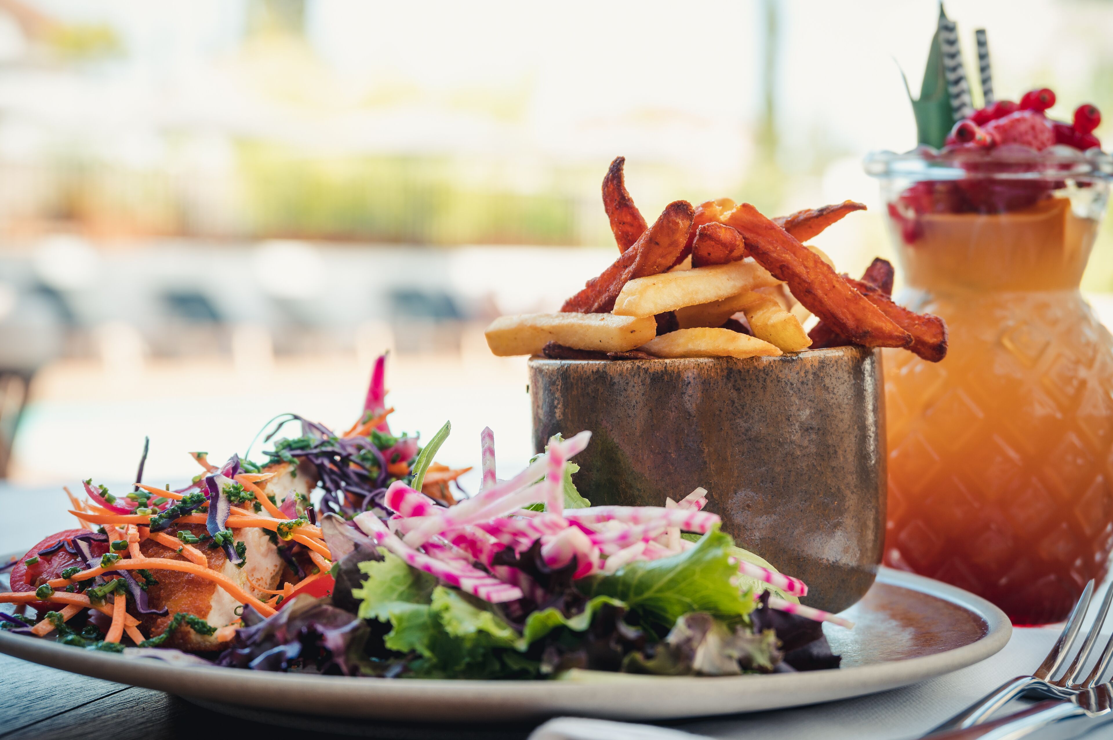 A meal with fries, a salad, and a drink on a wooden table.