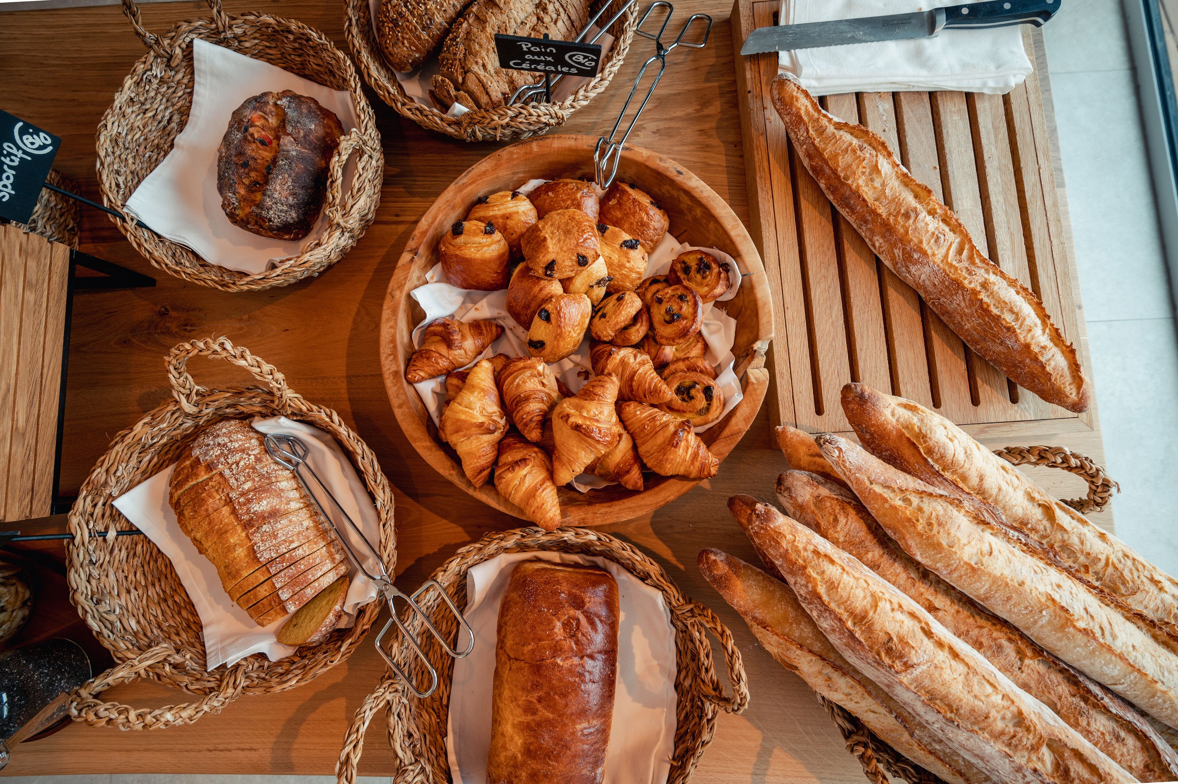 Une table en bois sur laquelle sont disposés des paniers contenant différents types de pain et de viennoiseries.