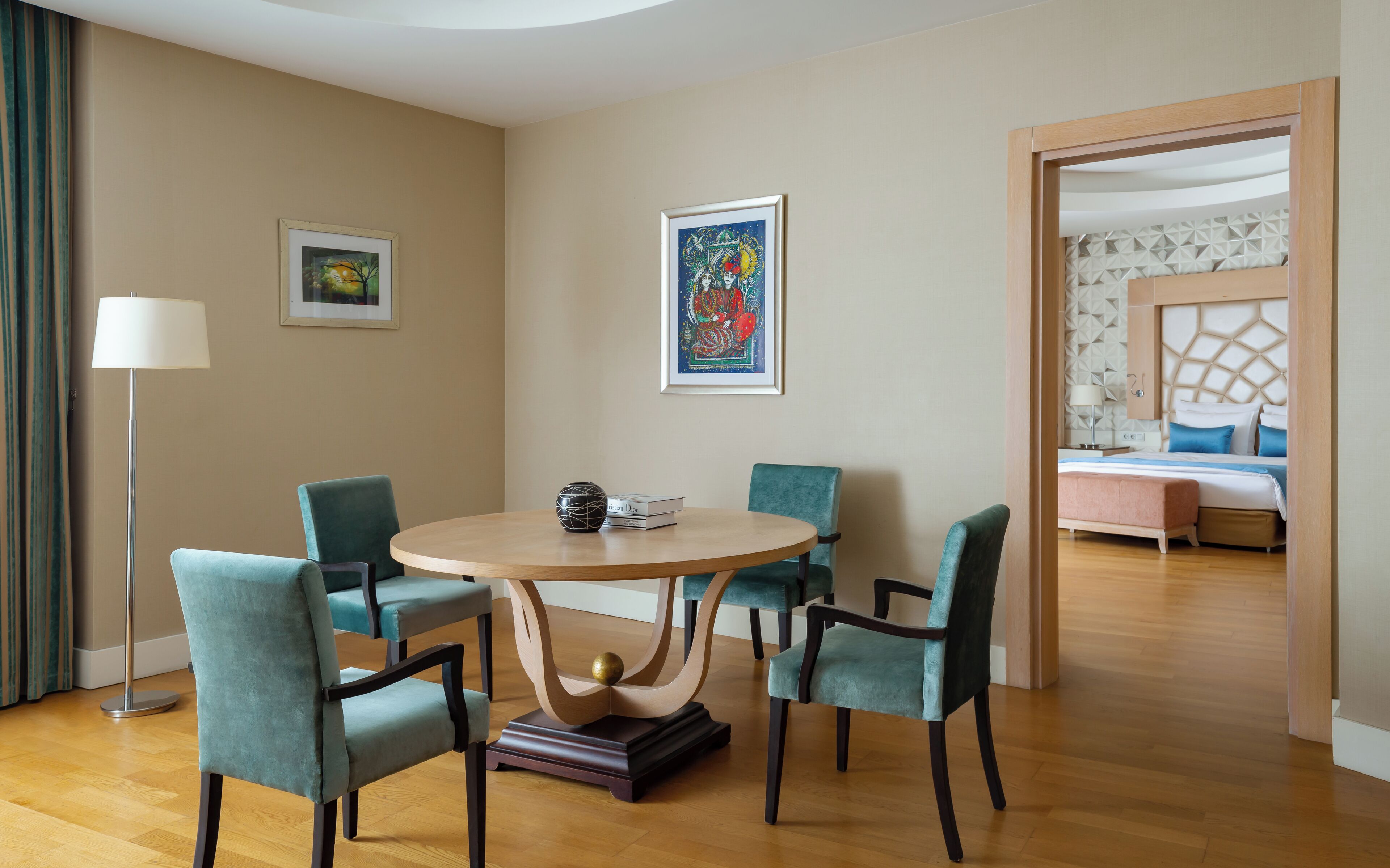 Quarto de hotel com uma mesa de jantar redonda, quatro cadeiras, um abajur e duas obras de arte emolduradas nas paredes.
