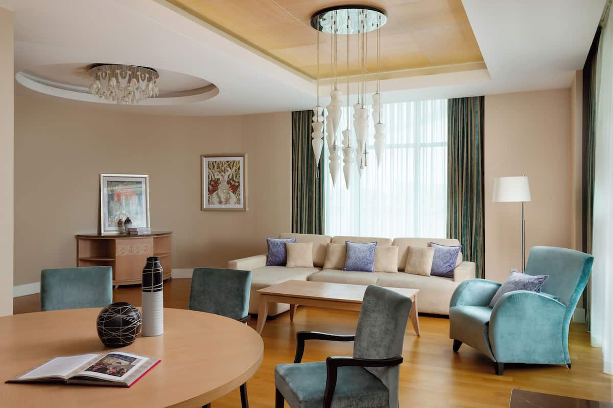 A modern living room with a sofa, chairs, a coffee table, and a dining table. There is a chandelier, artwork on the walls, and a lamp.