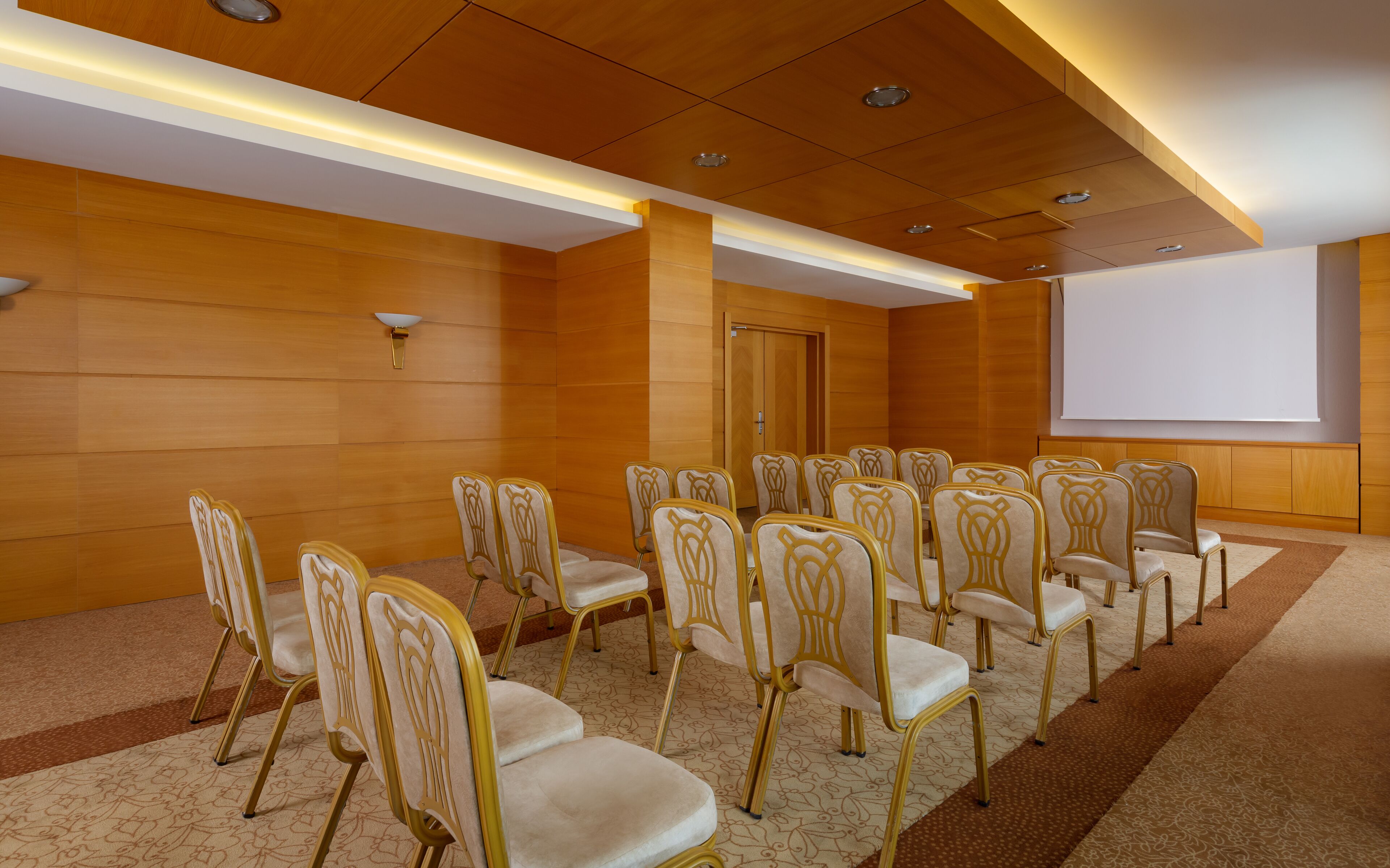 Une salle de conférence avec des rangées de chaises, un écran de projection et un lambris en bois.