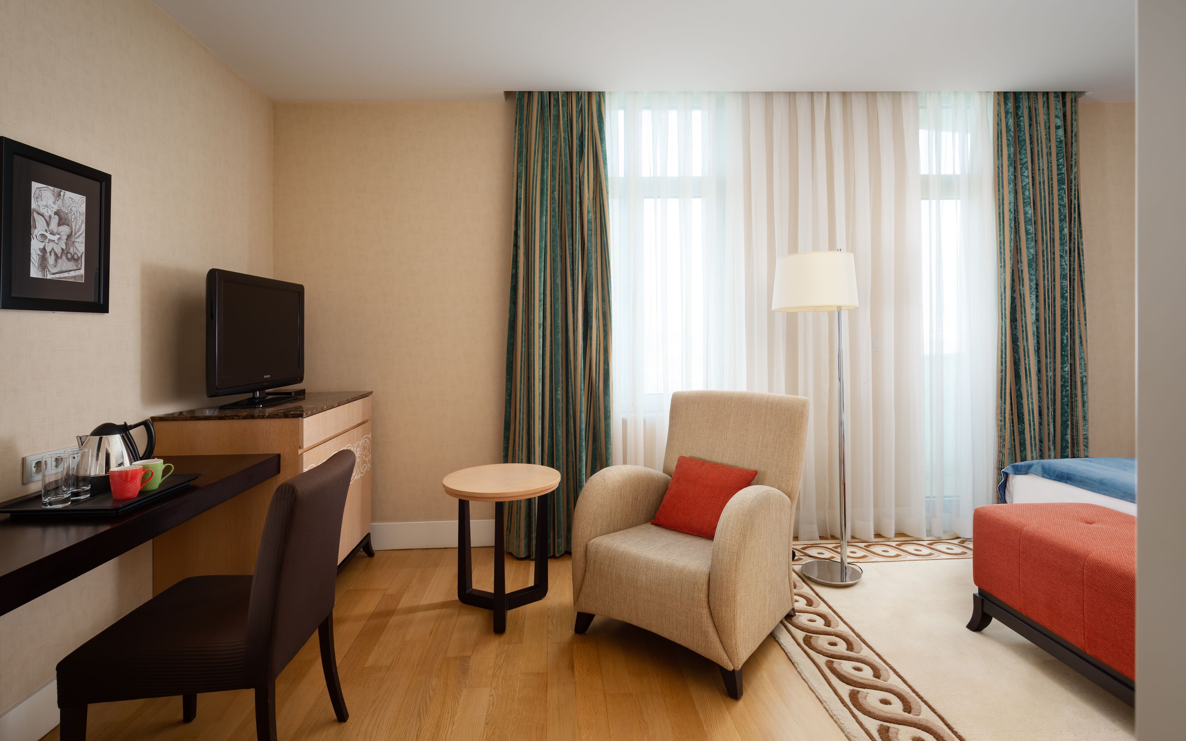 Ein Hotelzimmer mit Schreibtisch, Stuhl, Ohrensessel und Bett.