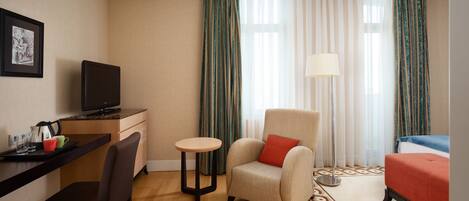 A hotel room with a desk, chair, armchair, and a bed.