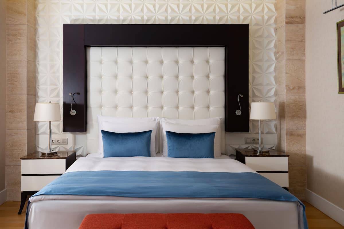 A bedroom with a tufted headboard, two bedside tables with lamps, a bed with blue and white bedding, and a red throw blanket.