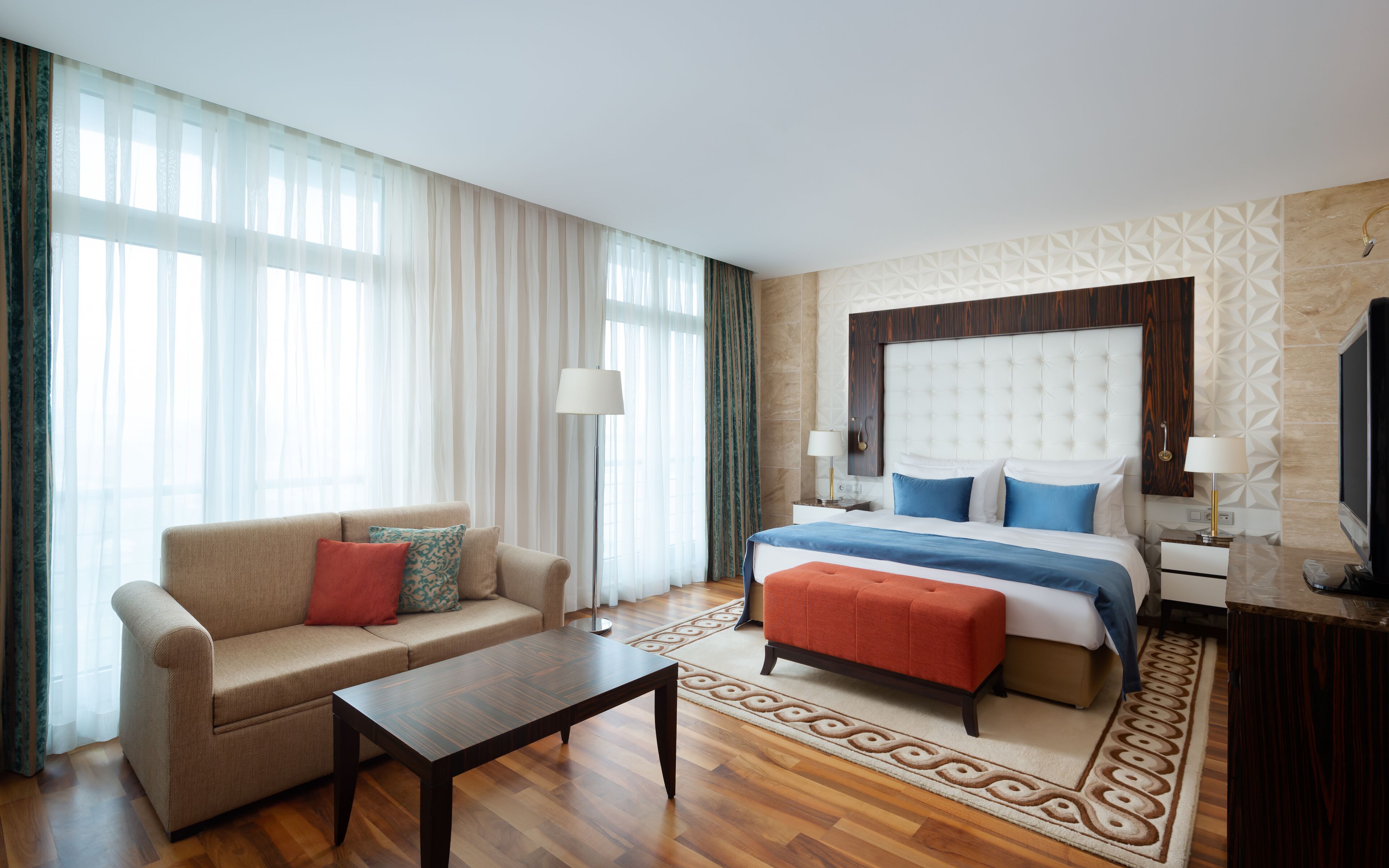 A hotel room with a bed, a sofa, a coffee table, and a TV.