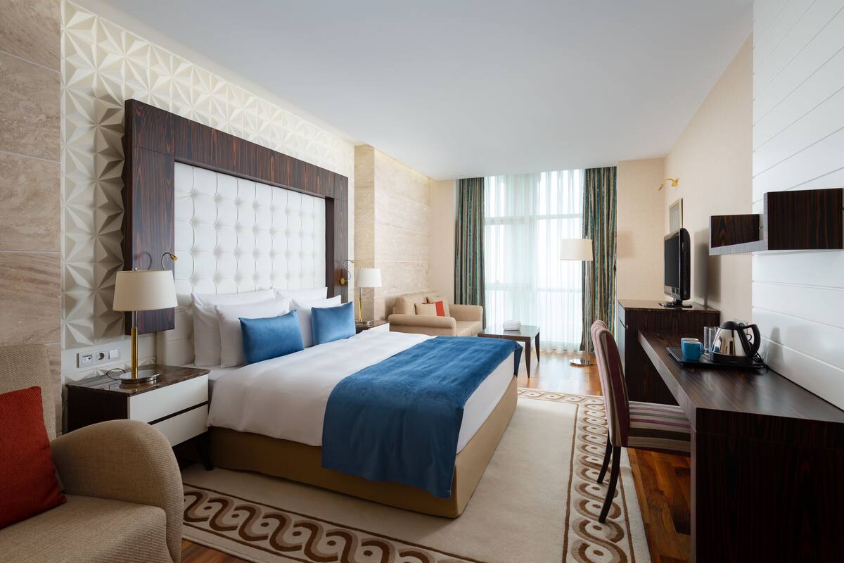 A hotel room with a large bed, a desk, a TV, and a sofa.