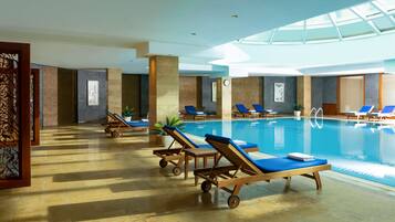 A spacious indoor swimming pool with multiple sun loungers and a glass ceiling.