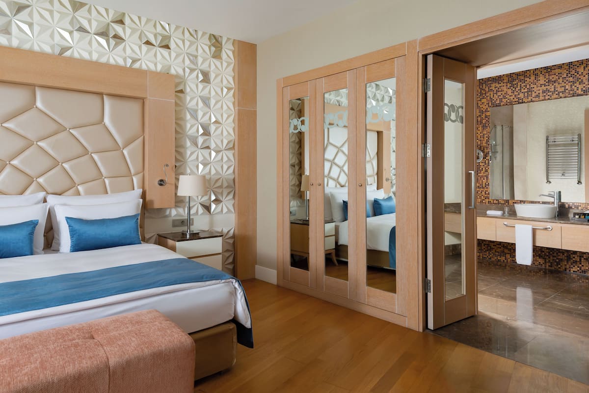 A hotel room with a large bed, a nightstand, a mirror, and a bathroom with a sink and mirror.