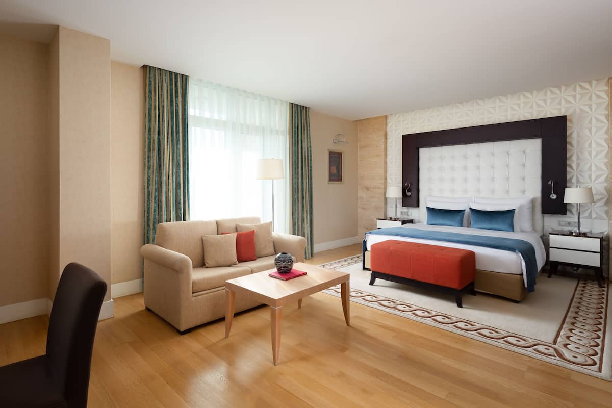 A hotel room with a bed, a sofa, a coffee table, a TV, and a desk.