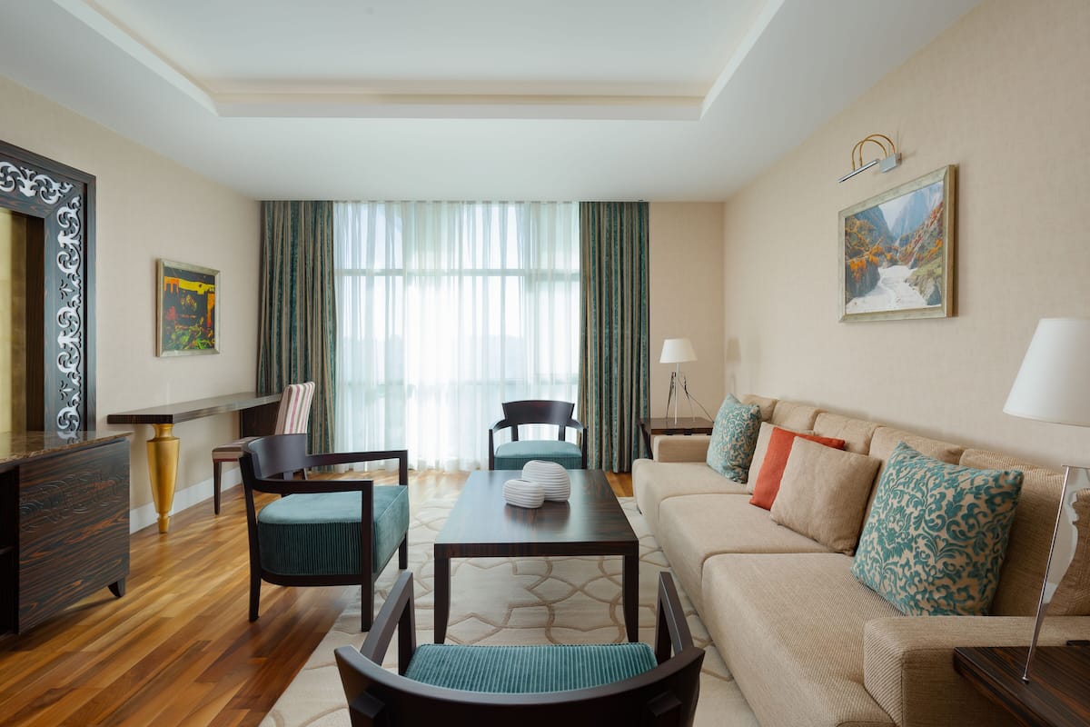 A modern hotel room with a wooden floor, a sofa with patterned cushions, a dining table, and a TV.