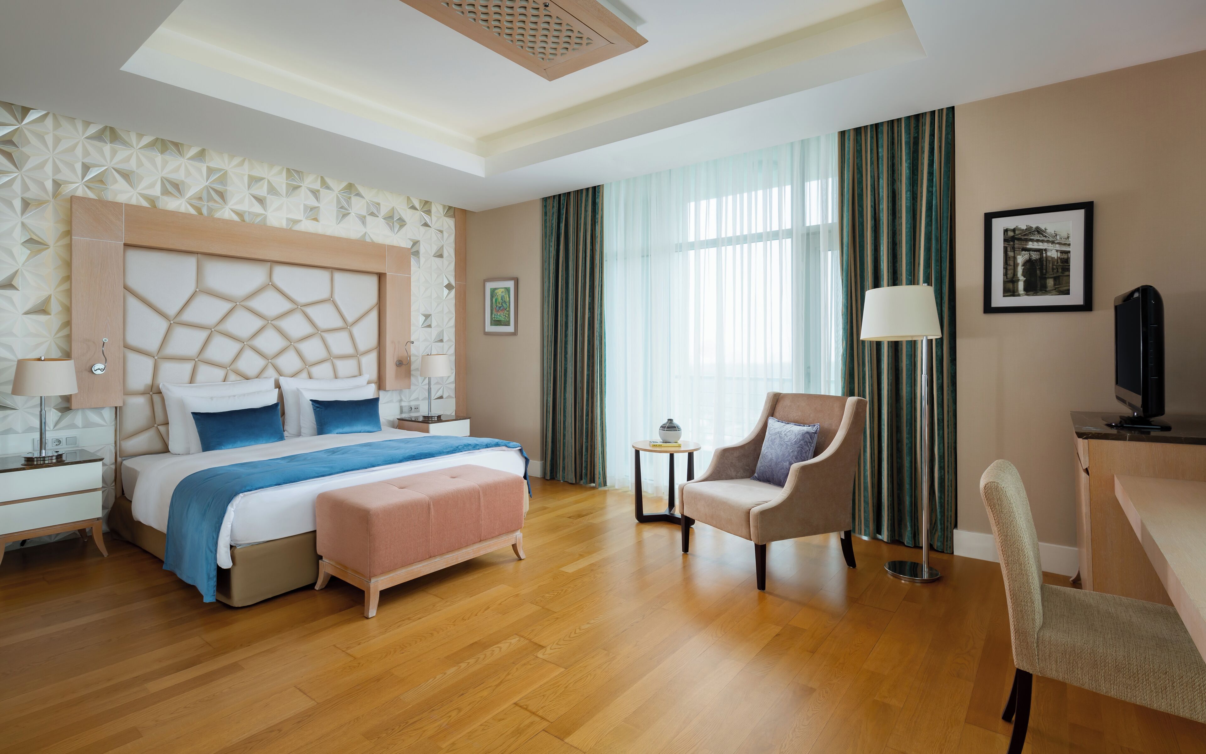 A hotel room with a bed, a desk, a chair, a lamp, and a picture on the wall.
