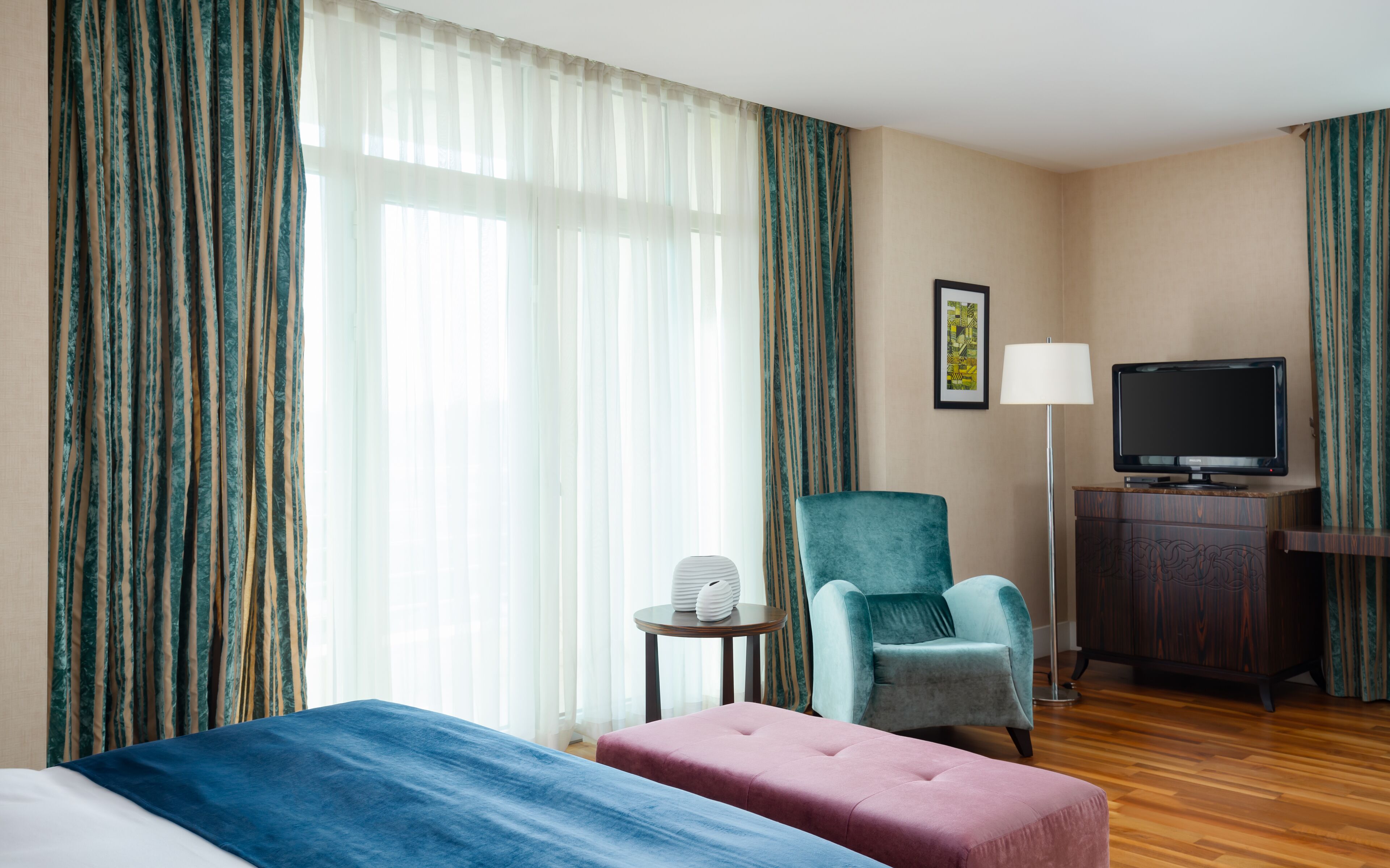 A hotel room with a bed, a chair, a TV, and a lamp.