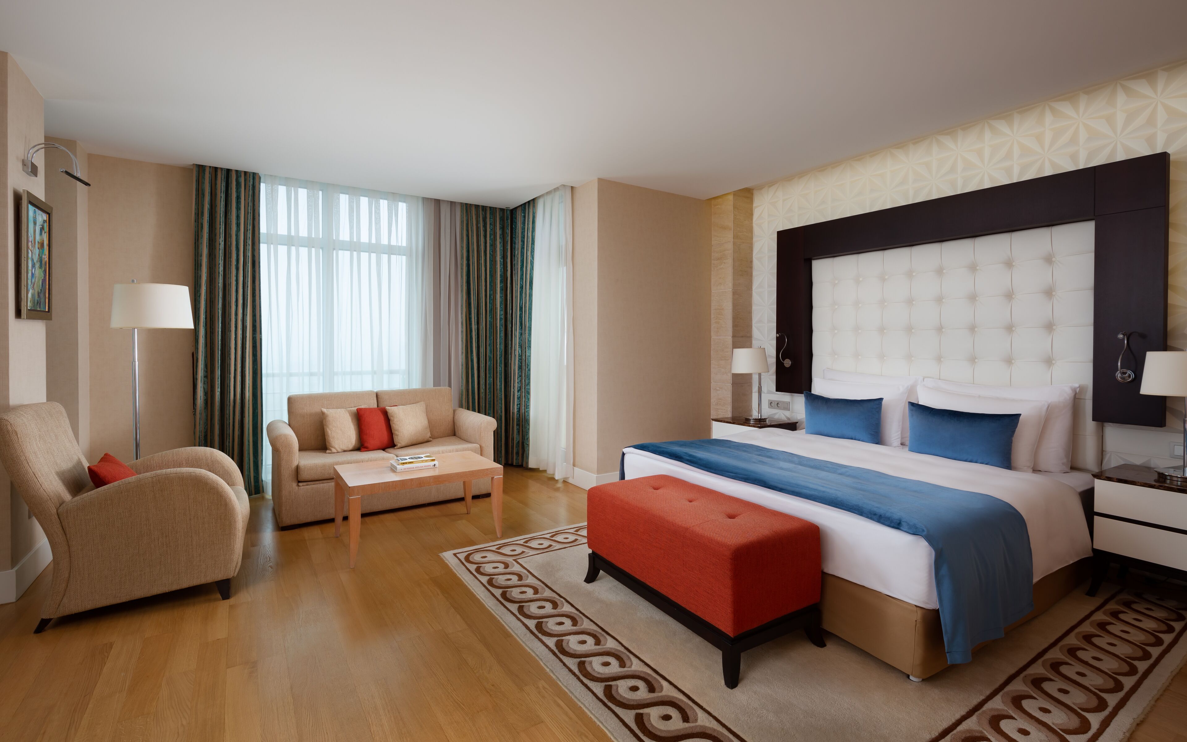 A hotel room with a bed, a sofa, a coffee table, a floor lamp, and a patterned rug.
