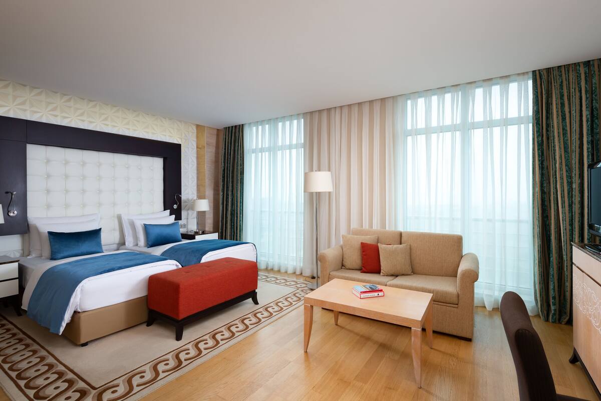 A hotel room with a large bed, a sofa, a coffee table, and a TV.