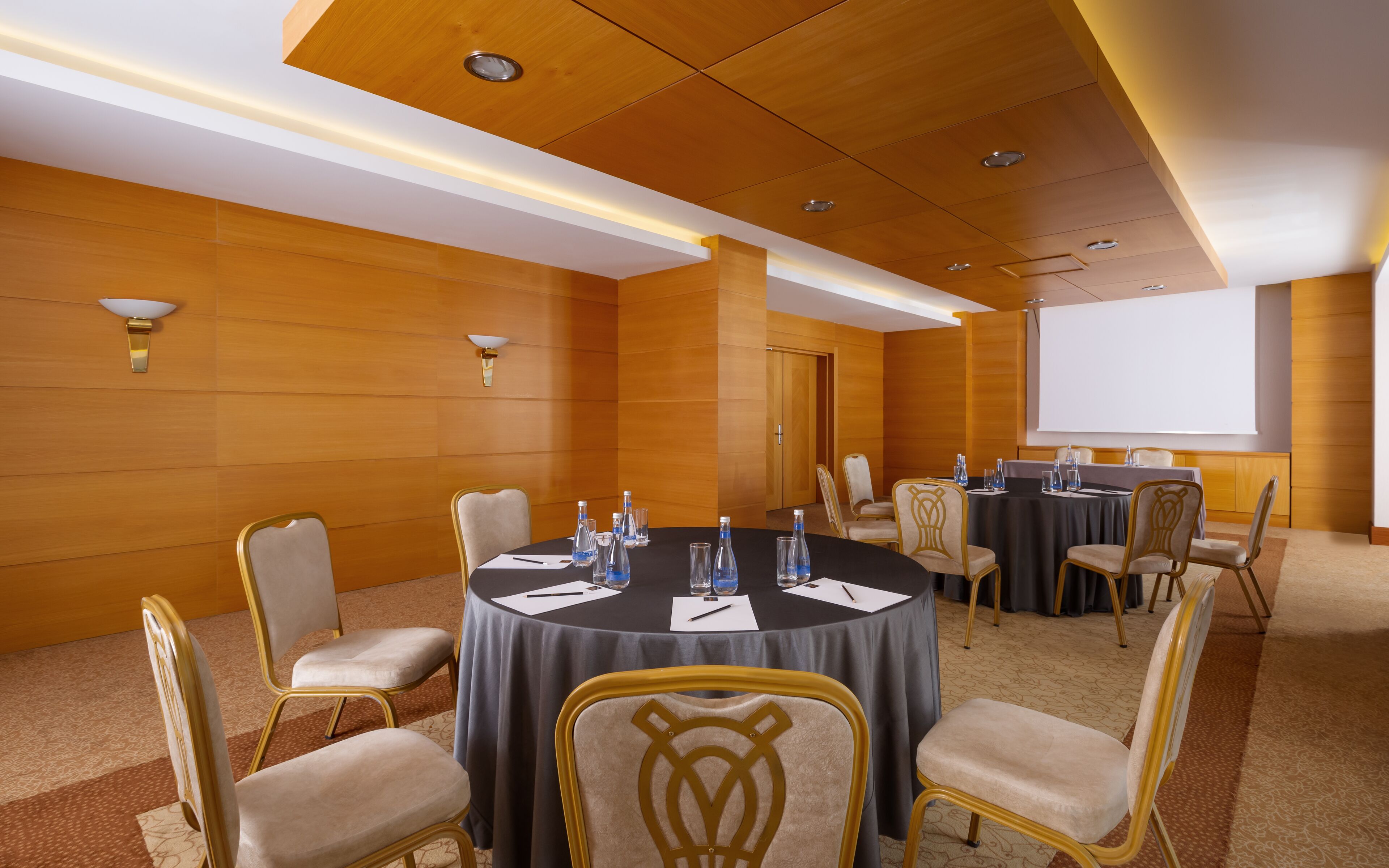 A conference room with round tables, chairs, and a projector screen.