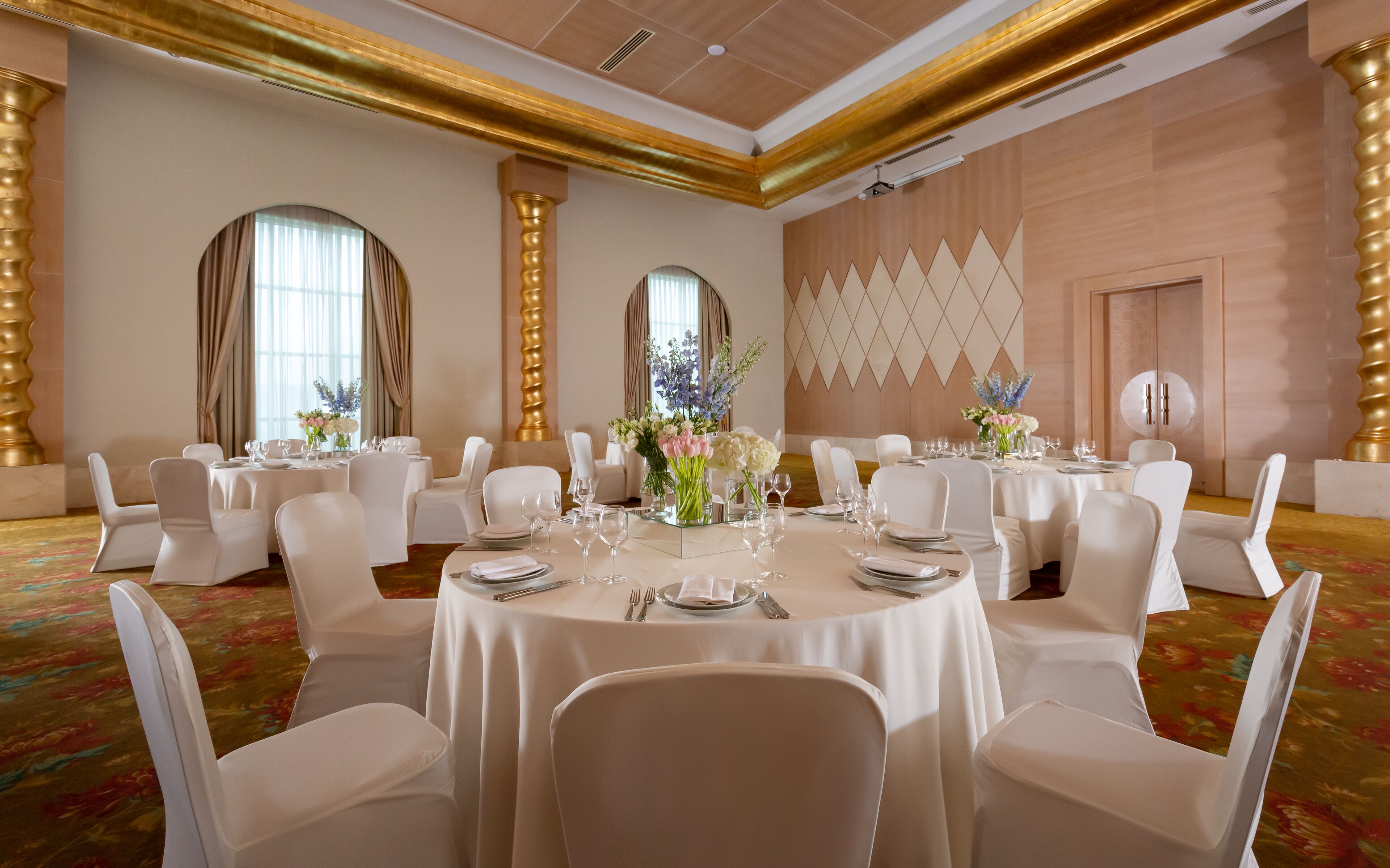 A banquet hall with round tables set for dining, white chairs, and floral centerpieces.