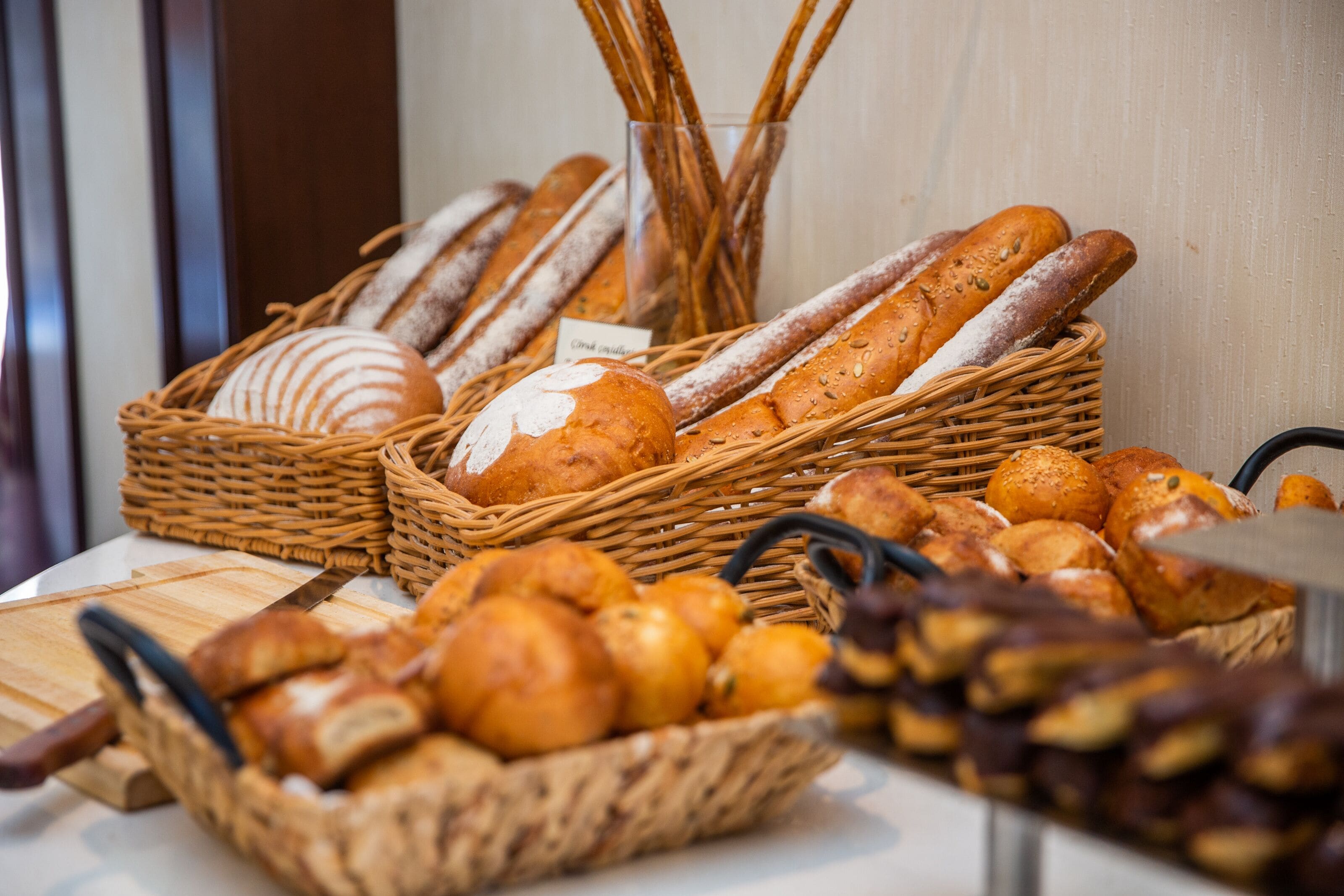 Verschiedene Brotsorten und Gebäck in Weidenkörben auf einem Tisch präsentiert.