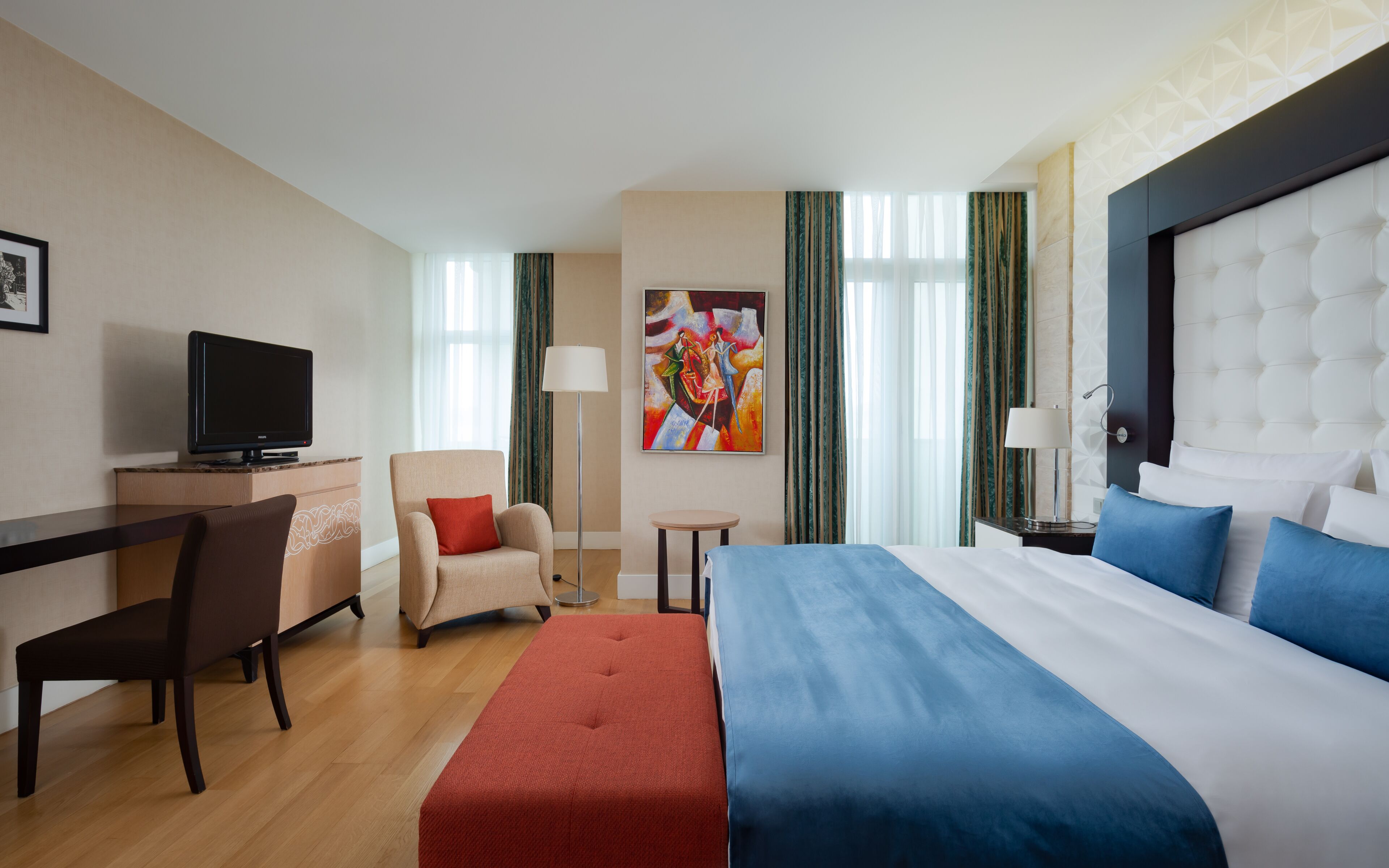 Een hotelkamer met een bed, een bureau, een stoel, een televisietoestel en een schilderij aan de muur.