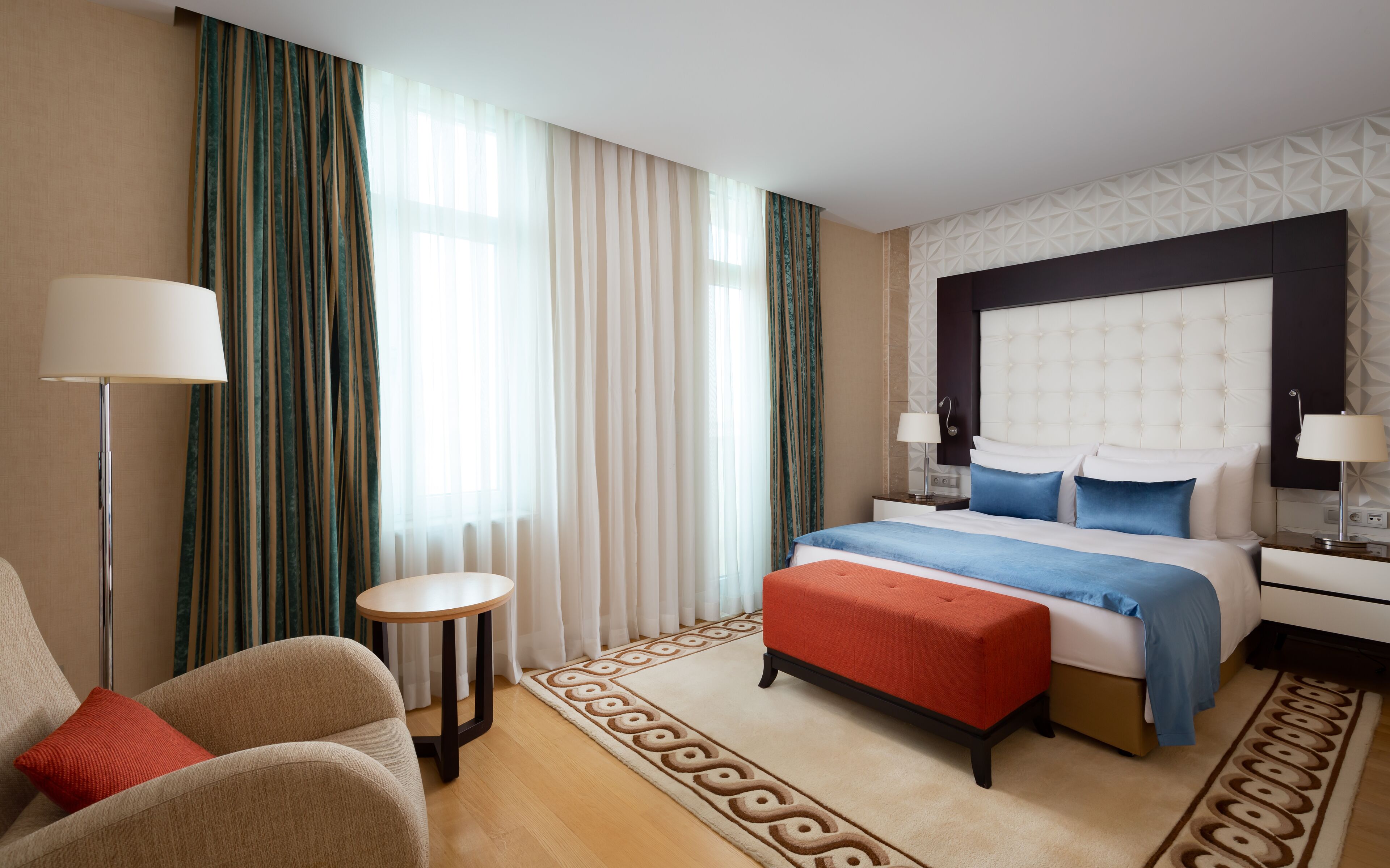 A hotel room with a bed, a chair, a side table, and a lamp.