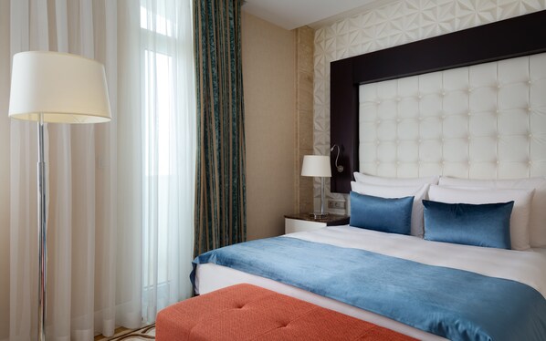 A hotel room with a large bed, a nightstand, a lamp, and a view of the outside through sheer curtains. - Badamdar Hotel and Residences (Baku)