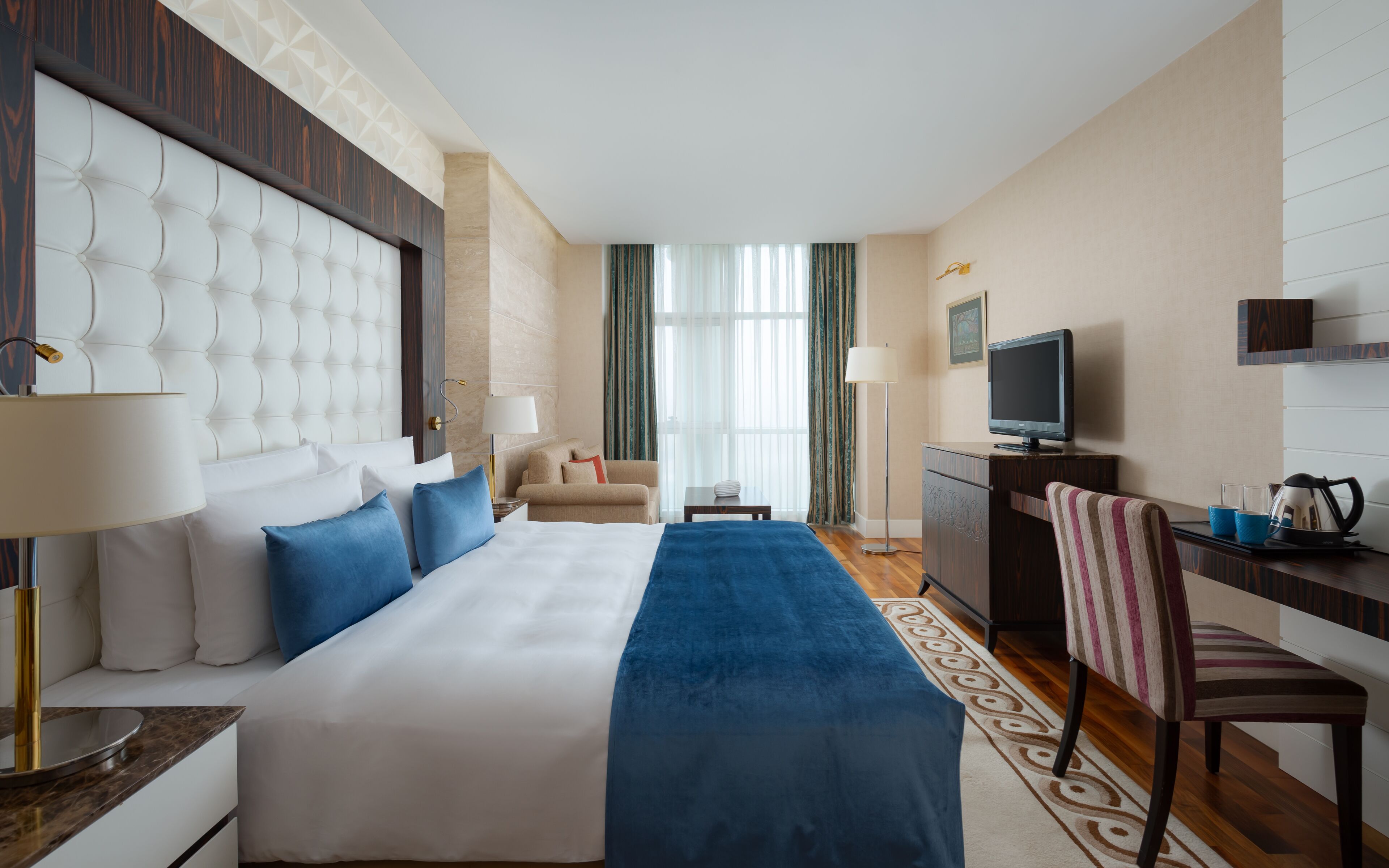 A hotel room with a large bed, a desk with a television, a chair, and a window with curtains.