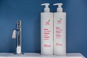 Two bottles of organic hair and body wash next to a chrome faucet on a white surface against a blue background. - Art Apartment at Sanit by Wonderful Italy (Naples)