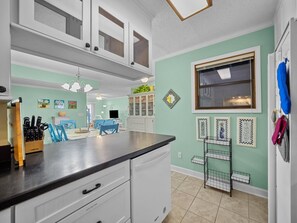 A kitchen with white cabinets, a black countertop, and a window with blinds. There are kitchen utensils on the counter and a small rack with dishes. - 3BR Oceanfront Condo in North Topsail Beach w/ Community Pool & Elevator (North Topsail Beach)