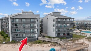 Un hotel frente al mar con varios balcones, piscina y un paseo marítimo de madera.