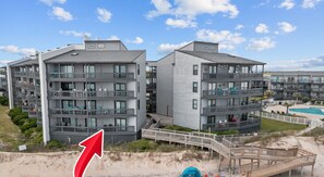 A beachfront hotel with multiple balconies, a pool, and a wooden boardwalk.