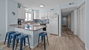 A modern kitchen with white cabinets, a granite countertop, and blue bar stools. - 3BR Oceanfront Condo with Community Pool (North Topsail Beach)