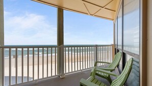 A balcony with a view of the beach, two green chairs, and a glass door. - 3BR Oceanfront Condo with Community Pool (North Topsail Beach)