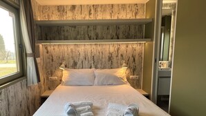 A neatly made bed with pillows, a bedside lamp, and slippers on the bed. -  Agricampeggio Le Bucoliche (Lazise)