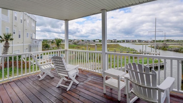 En overdækket terrasse med hvide Adirondack-stole og udsigt til en flod og bygninger i baggrunden.